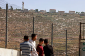 Palestinian schoolchildren stand at the courtyard of a school in the West Bank village of Urif, south of the northern city of Nablus, backdropped by buildings of the Israeli settlement of Yitzhar 